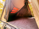 RV rental adventure: Comfy rooftop tent interior with dark mattress, storage pockets, and mesh panels overlooking the forest.