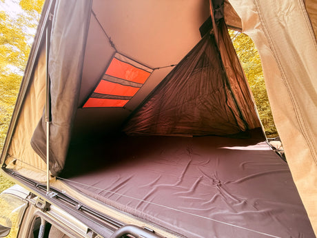 RV rental adventure: Comfy rooftop tent interior with dark mattress, storage pockets, and mesh panels overlooking the forest.