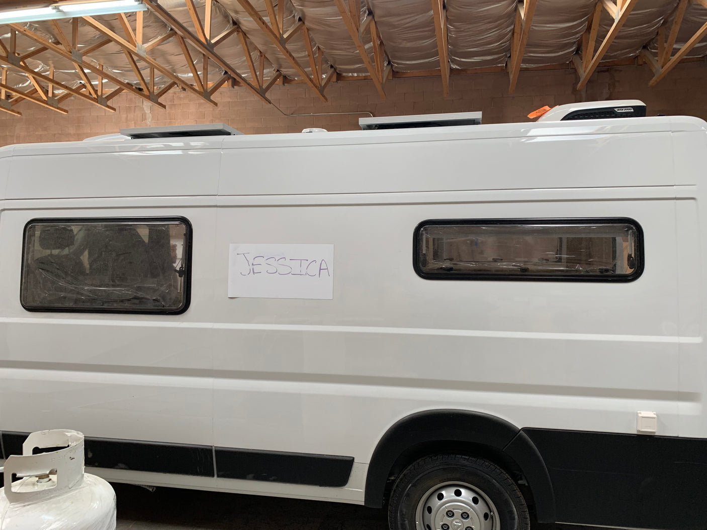 New white RV rental van, possibly a camper conversion, with "JESSICA" sign & rooftop AC unit.