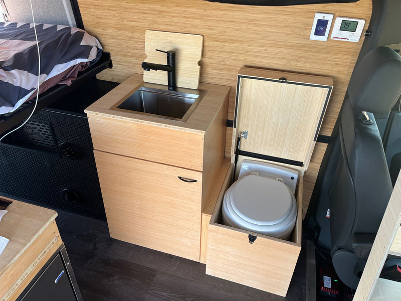 Inside a modern RV rental: Bamboo-lined camper van with bed, kitchenette sink, and pull-out toilet. Compact living amenities. — photo 10