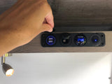 Hand on an RV rental's interior power panel, showing USB charging, a 12V socket, and a 14.8V DC voltage display.