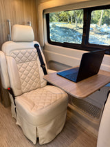 This RV rental features a cozy mobile office: a quilted cream seat, laptop on a table, and a beautiful outdoor view from the window.
