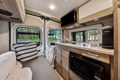 Cozy RV rental interior with a compact kitchen, comfortable seating, and TV, offering views of nature.