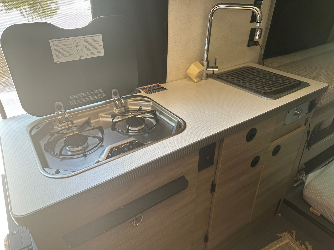 Compact RV rental kitchen featuring a two-burner stove, sink with faucet, and counter. Perfect for camping meals. — photo 7