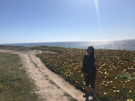 A person on a dirt coastal path with ocean, flowers. Explore scenic views with an RV rental.