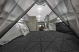 Cozy RV rental interior with a bed, dark comforter, mosquito net, and a glimpse of the kitchen area.