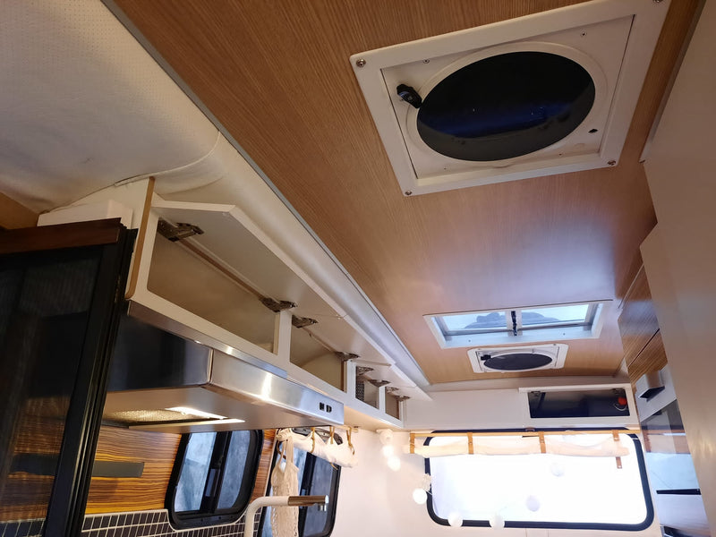 Inside an RV rental: view of light wood ceiling, open overhead storage, modern range hood, and roof vents, for a cozy camper feel. — photo 16