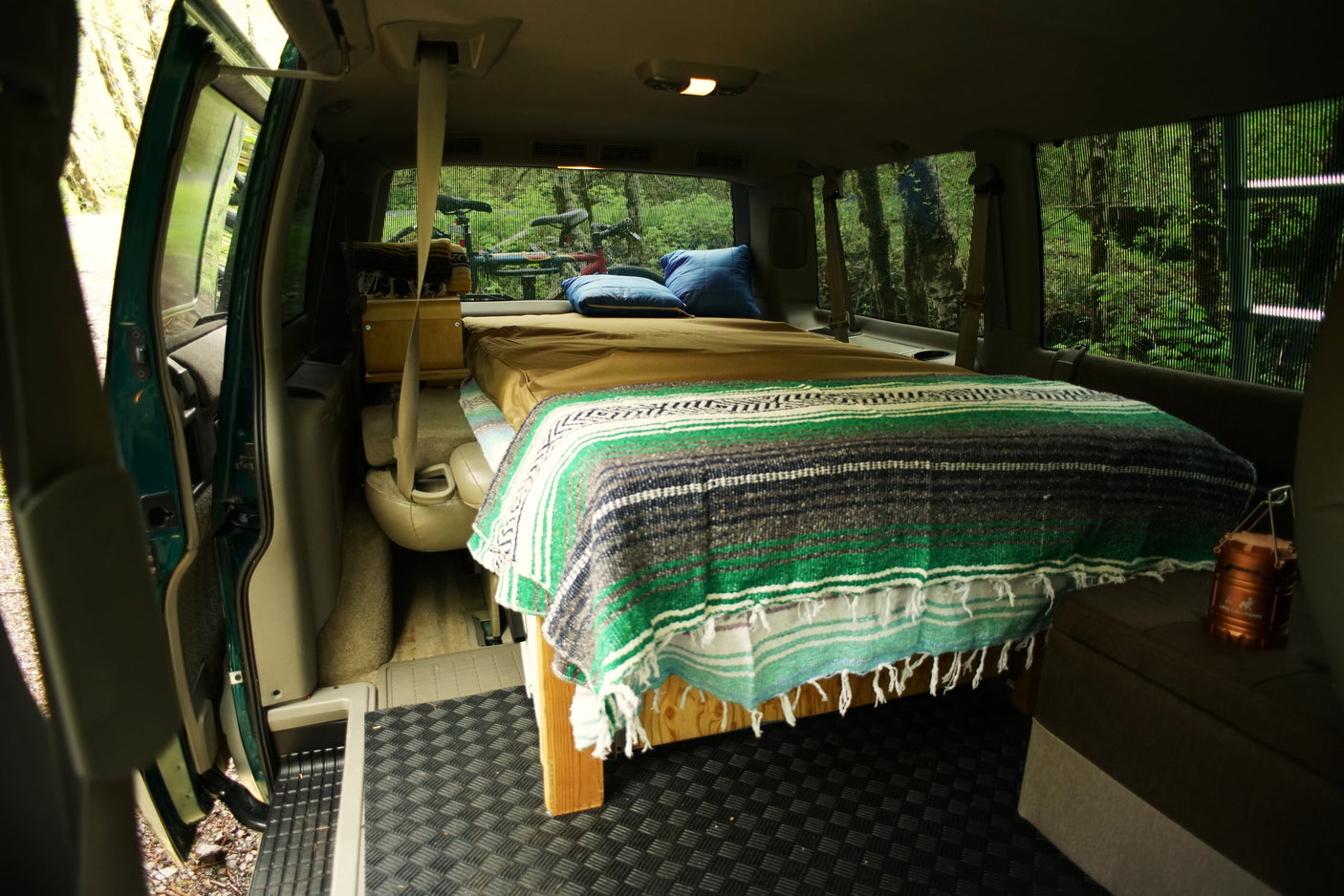 Cozy camper van interior: bed, pillows, bike, forest view. Perfect for RV rental adventures.