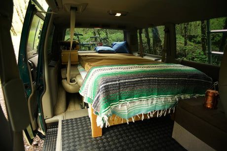 Cozy camper van interior: bed, pillows, bike, forest view. Perfect for RV rental adventures.