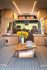 This RV rental interior features a stylish kitchen, dining area with sunflowers, and comfortable seating, ideal for mobile living.