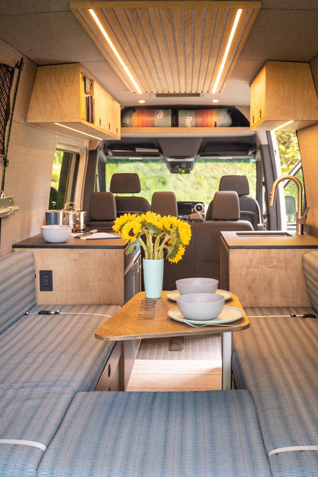 This RV rental interior features a stylish kitchen, dining area with sunflowers, and comfortable seating, ideal for mobile living.