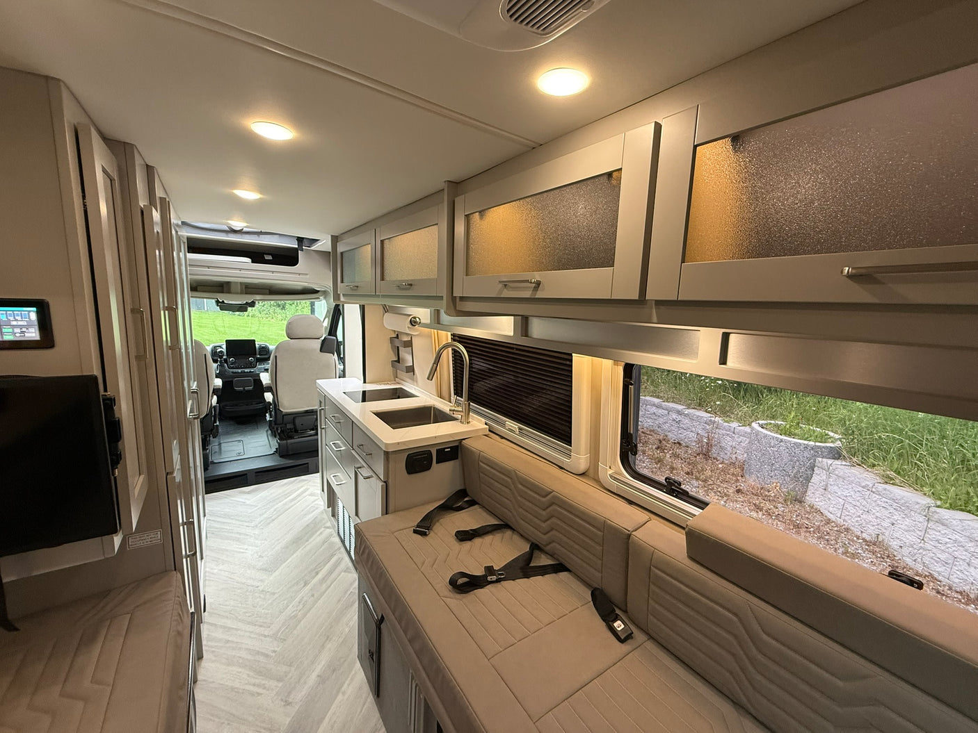 Bright RV rental interior showing a modern kitchen, comfortable seating with belts, and stylish frosted overhead cabinets.