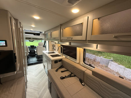 Bright RV rental interior showing a modern kitchen, comfortable seating with belts, and stylish frosted overhead cabinets.