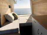 Cozy RV rental interior featuring wooden walls, soft cushions, and a stunning ocean view. Perfect for your next van life trip.
