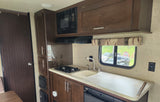 RV rental kitchen with microwave, sink, stovetop, and cabinets. A window offers a view of the outdoors.