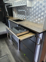 Sleek RV rental interior: modern kitchen with wood counters, sink, pull-out induction cooktop, and accent lighting.