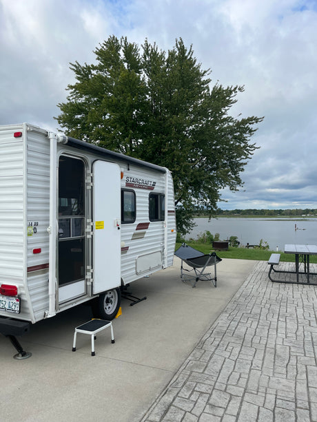Starcraft travel trailer at a serene rv rental campsite, featuring a grill, picnic table, and scenic lake view.