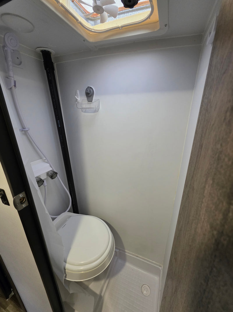 This RV rental bathroom features a compact wet bath with a toilet, handheld shower, and ceiling vent fan. — photo 5