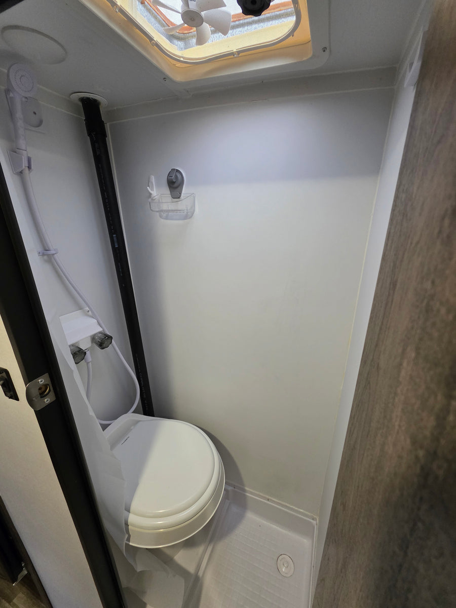 This RV rental bathroom features a compact wet bath with a toilet, handheld shower, and ceiling vent fan.