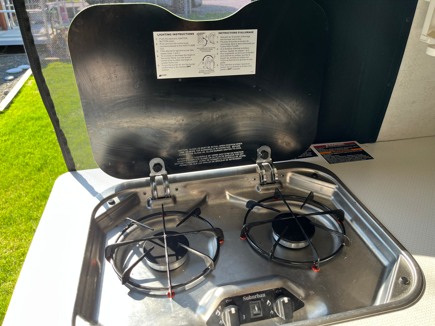 Two-burner gas stove with open glass lid showing lighting instructions in an RV rental kitchen.