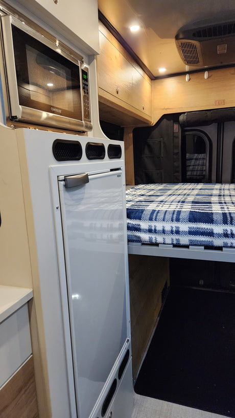 RV rental interior: cozy bed, microwave, and fridge. Designed for comfort and convenience in a compact living space.