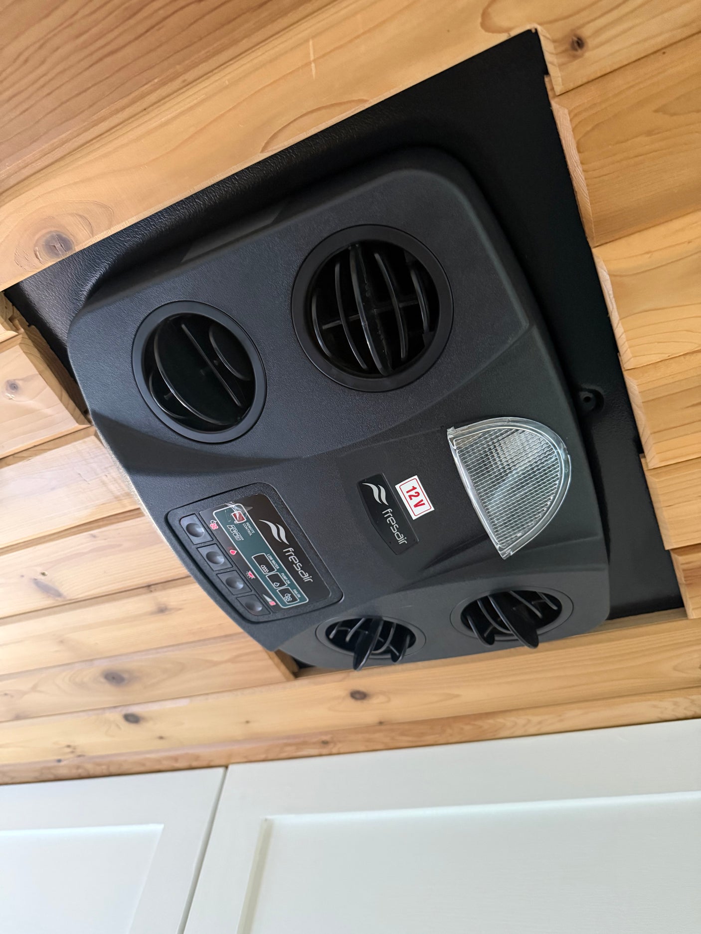 Overhead Fresair 12V cooling unit with adjustable vents, control panel & light in an RV rental. Enhances cabin comfort.