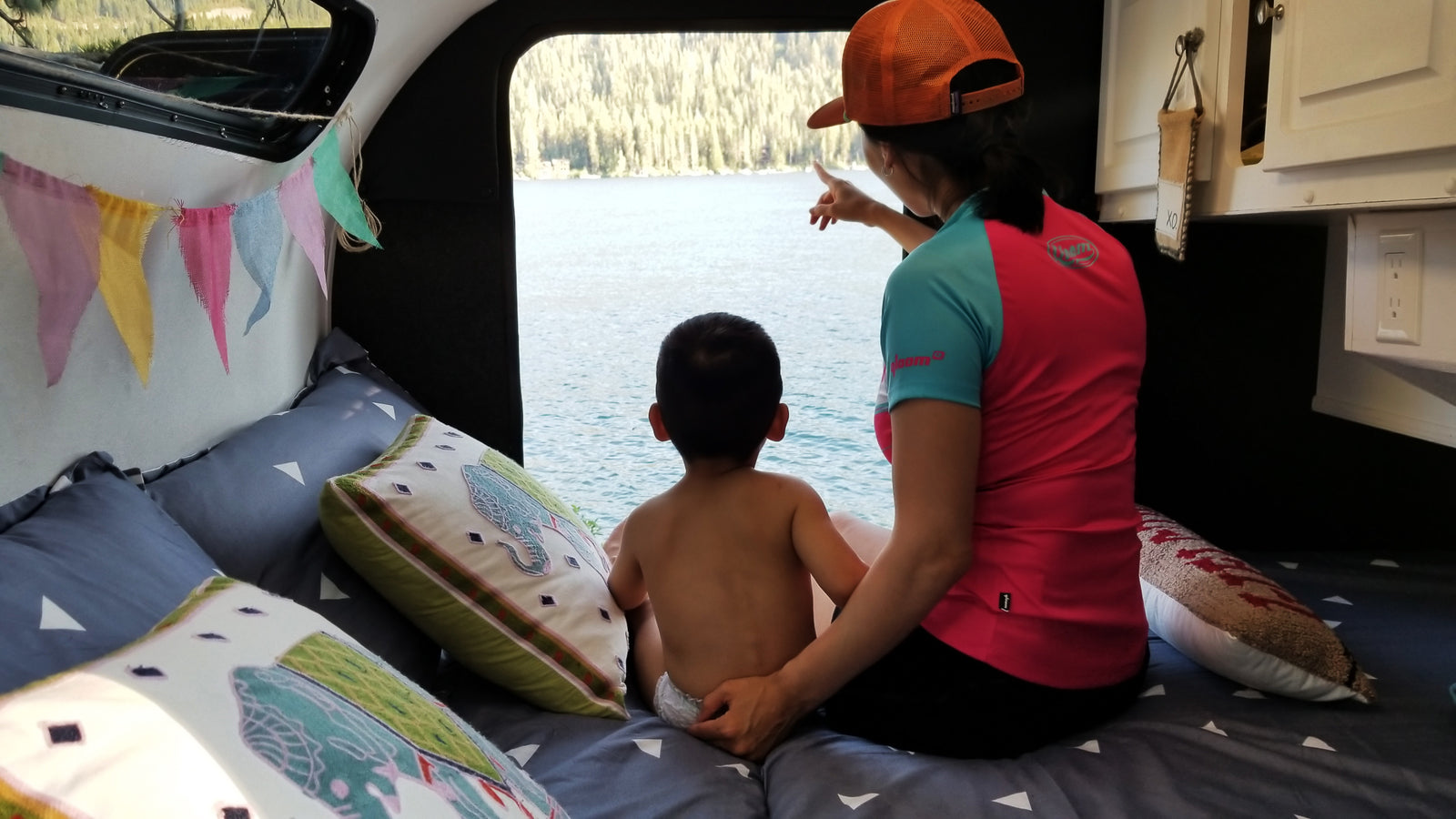 RV rental: A cozy family moment inside, watching the beautiful lake view. Mom points out details to child from bed.