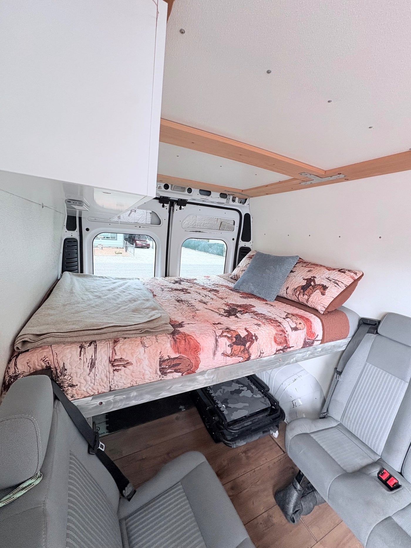 Cozy rv rental camper van interior: elevated bed with western quilt, passenger seating, and under-bed storage. — photo 4