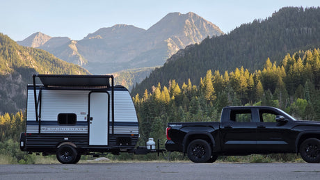 Black Toyota Tundra towing a Springdale RV rental in a scenic mountainous, forested landscape. Ideal for outdoor adventures.