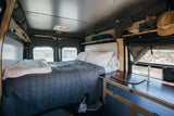 Cozy RV rental interior with bed, kitchenette, and desert views, perfect for a road trip adventure.