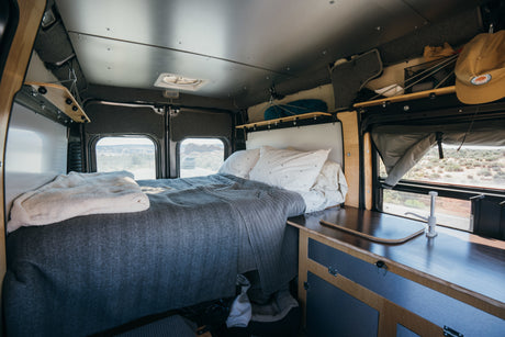 Cozy RV rental interior with bed, kitchenette, and desert views, perfect for a road trip adventure.