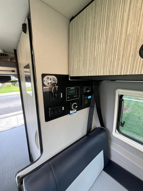 Inside this RV rental, see the main utility control panel, comfortable seating with seatbelt, and overhead storage. Ready for travel.