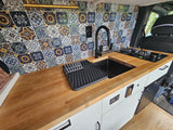 Stylish RV rental kitchen with vibrant tile backsplash, wooden counters, black sink & cooktop, ideal for travel.