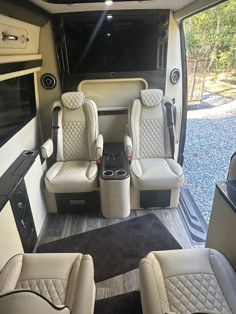 Luxury RV rental cabin: spacious interior with plush cream captain's chairs, center console, and wall-mounted TV.