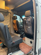 Inside an RV rental: swivel front seats with attached Carhartt organizers, custom overhead storage, & wood floor.