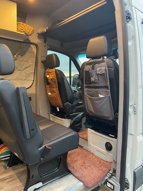 Inside an RV rental: swivel front seats with attached Carhartt organizers, custom overhead storage, & wood floor.