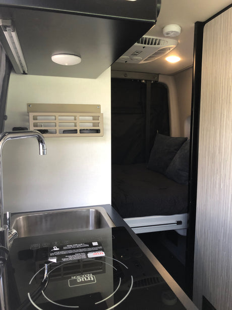 This RV rental shows a compact interior with a modern kitchen, featuring a sink and True Induction cooktop, alongside a comfy sleeping area.