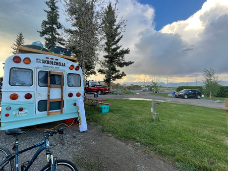 Light blue and white Skoolie (converted school bus) at a scenic campground. Ideal for your next RV rental adventure.