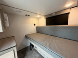 This modern RV rental interior features a versatile bench bed, overhead lighting, and compact storage, ideal for travel.