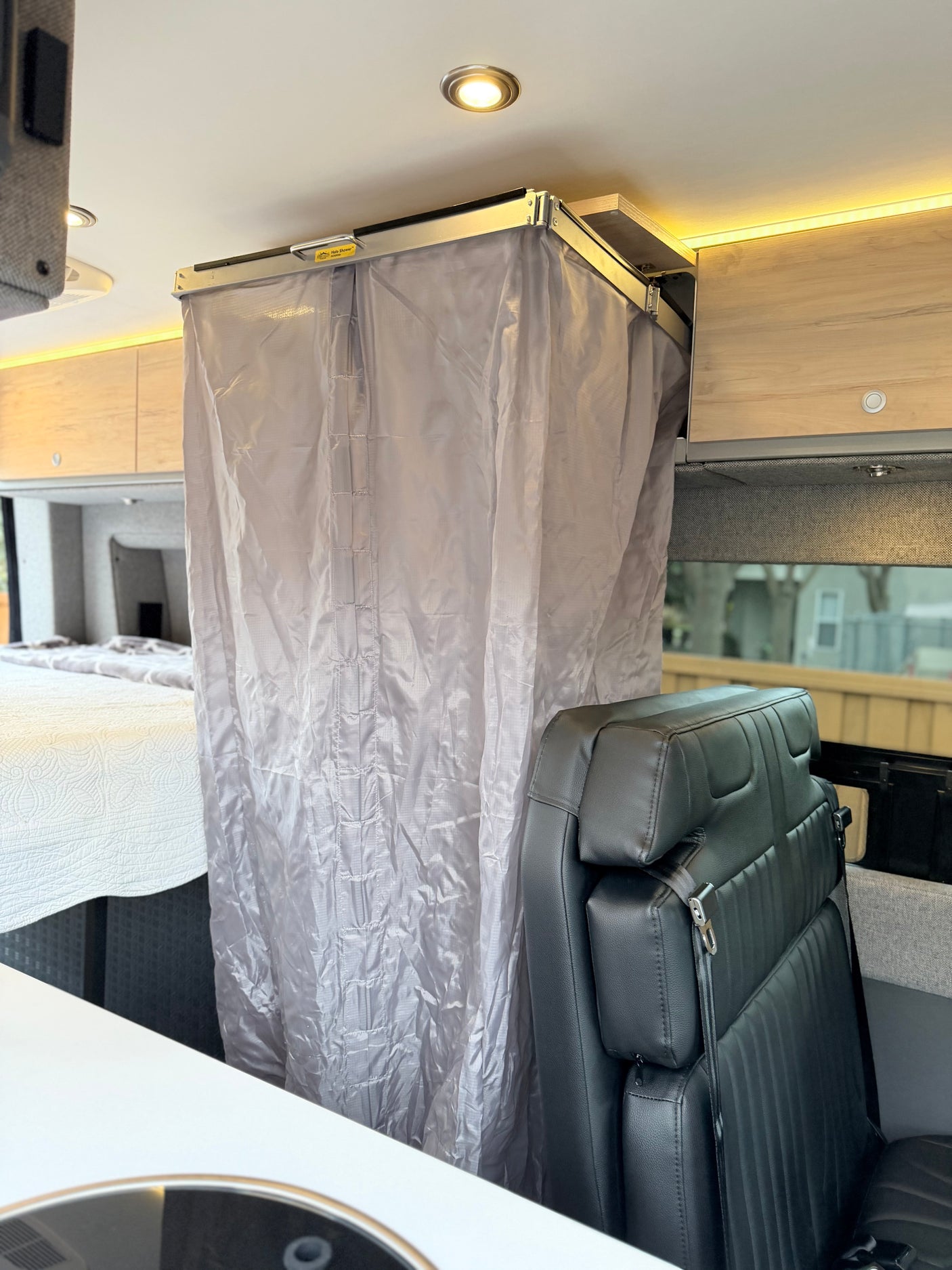RV rental interior featuring a gray compact shower curtain, black leather seat, and a comfy bed for convenient travel.