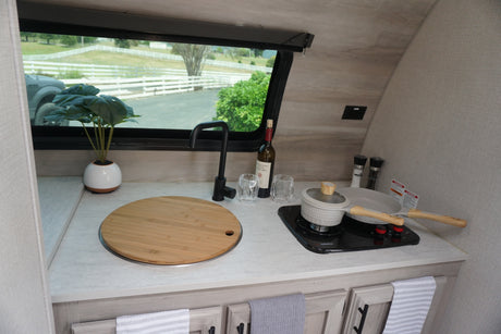 Get cooking in this cozy RV rental kitchen, featuring a sink, stovetop, and cookware. View of white fences outside.