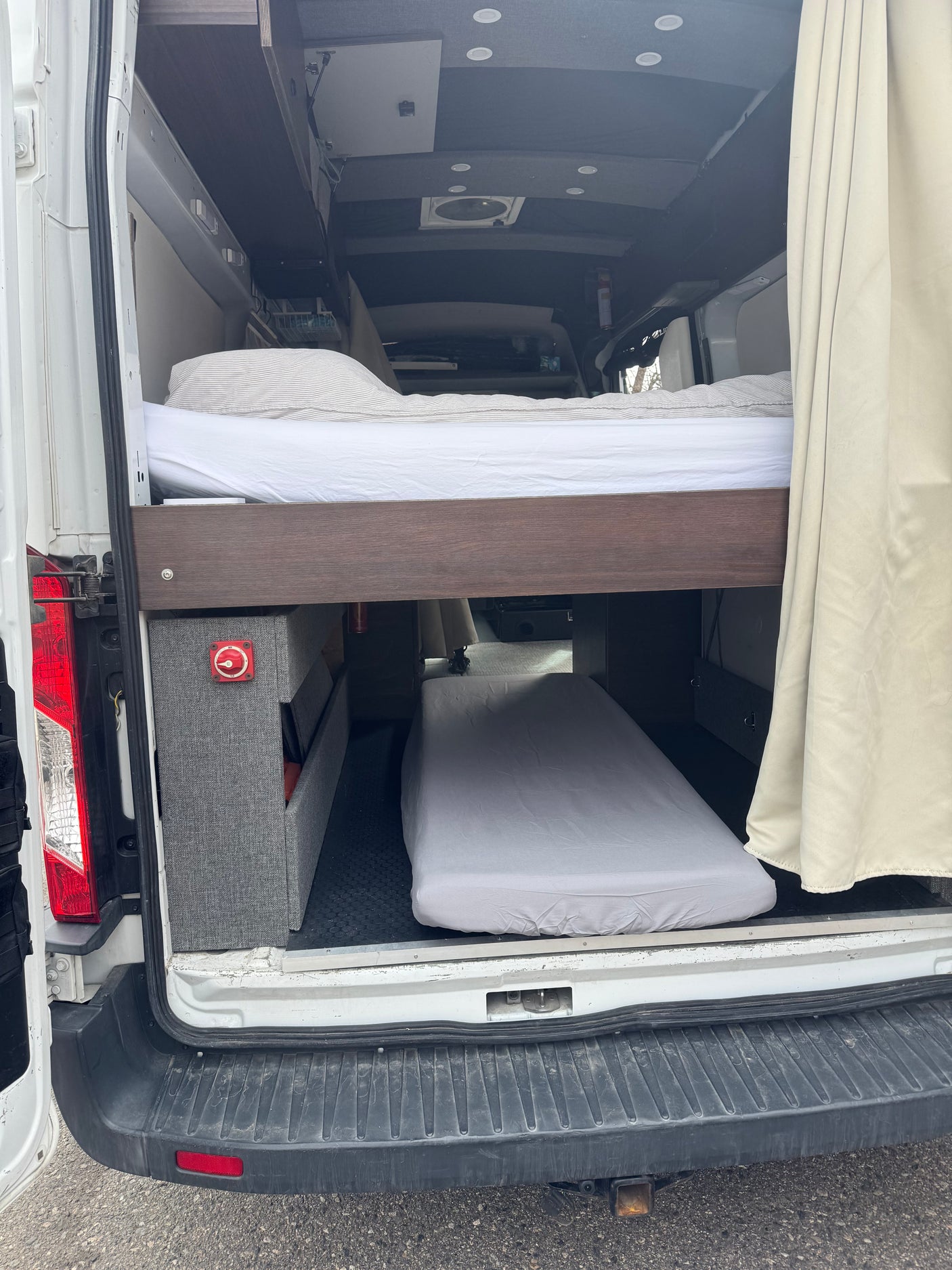 View inside an RV rental camper van showing bunk beds, storage, and battery disconnect switch from the back.