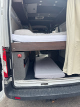 View inside an RV rental camper van showing bunk beds, storage, and battery disconnect switch from the back.