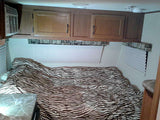 This cozy RV rental bedroom features a zebra comforter, overhead cabinets, and AC. Ideal for travel accommodation.