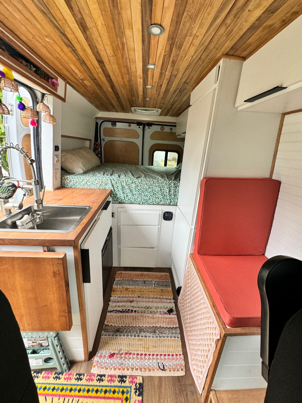 Step inside this cozy RV rental! Features a full kitchen, comfy bed, and seating area in a wood-paneled camper van.