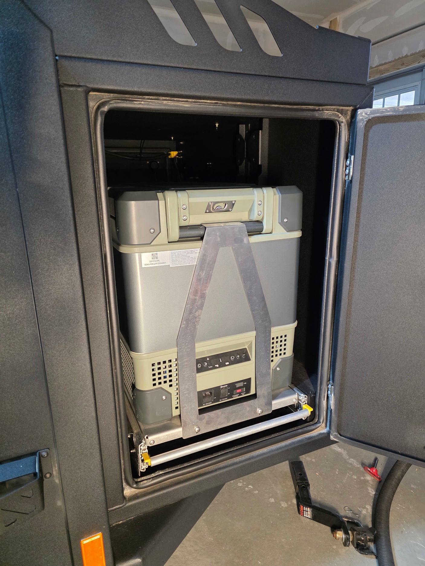 Portable refrigerator on a sliding tray inside an RV rental camper's open compartment, ready for outdoor adventures.