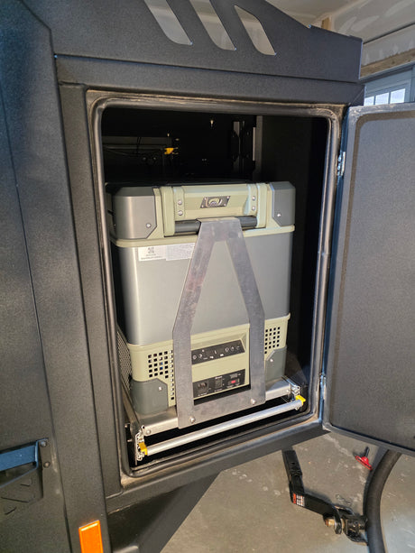 Portable refrigerator on a sliding tray inside an RV rental camper's open compartment, ready for outdoor adventures.