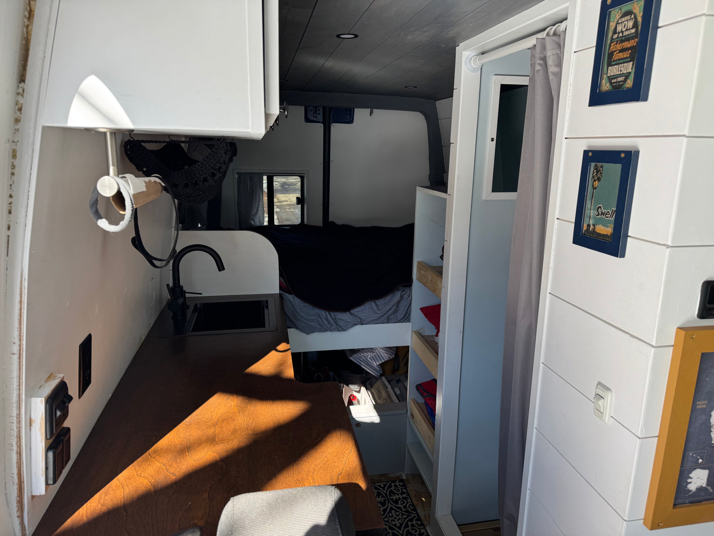 This cozy RV rental interior features a compact kitchenette with a sink & faucet, wooden counter, and a bed in the rear, perfect for van life.