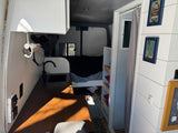 This cozy RV rental interior features a compact kitchenette with a sink & faucet, wooden counter, and a bed in the rear, perfect for van life.
