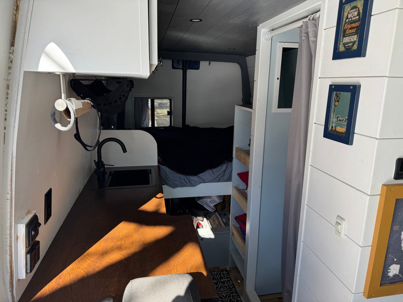 This cozy RV rental interior features a compact kitchenette with a sink & faucet, wooden counter, and a bed in the rear, perfect for van life. — photo 7